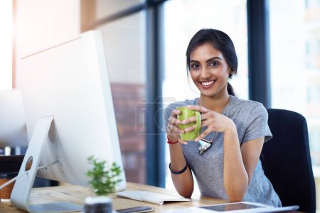 Foto de Café, computadora y retrato de la mujer india creativa en la oficina con confianza, relajarse y sonreír al inicio. Diseño, orgullo y cara feliz de desarrollador en línea con consultor profesional en el descanso - Imagen libre de derechos