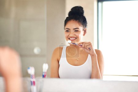 Téléchargez les photos : Miroir, soins dentaires et femme avec brosse à dents dans la salle de bain pour la routine des dents d'hygiène du matin. Sourire, bien-être et femme avec un produit de santé buccodentaire pour plaque, gencives et haleine fraîche à la maison - en image libre de droit