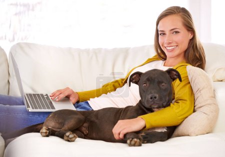 Téléchargez les photos : Portrait, femme et ordinateur portable par chien sur canapé, canapé et détendez-vous à la maison avec la technologie, Internet et connexion pour blog en ligne. Femme, animal et sourire dans le salon, la maison et l'appartement. - en image libre de droit