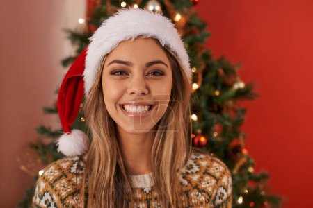 Glückliche Frau, Porträt und Weihnachtsbaum mit Hut für festliche Stimmung, Dezember Urlaub oder Jahreszeit zu Hause. Gesicht einer jungen weiblichen Person mit Schlägen für den Weihnachtsmann, Feier oder Bescherung mit Hausdekoration.