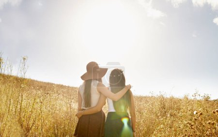Photo for Friends, walking and hug in summer nature on holiday or journey on vacation for adventure. Women, back and embrace outdoor together in sunshine on field, trekking on hill or travel environment. - Royalty Free Image