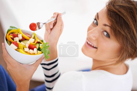 Téléchargez les photos : Femme, salade et portrait heureux avec des aliments sains pour l'alimentation, la désintoxication et le petit déjeuner sur le canapé à la maison. Détendez-vous et mangez des légumes, de la laitue et des repas verts ou végétaliens dans un bol pour la nutrition et le bien-être. - en image libre de droit