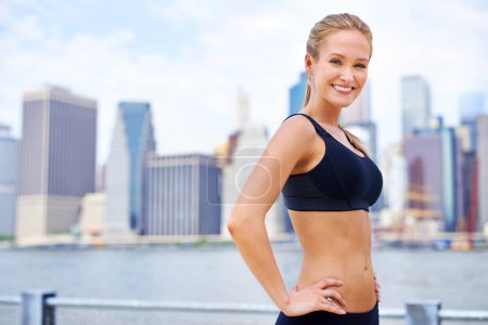 Photo for Woman, city and confident at river in sportswear with break for walk, fitness and healthy mindset in New York. Portrait, female person and smile with self care in summer, hot weather and happy. - Royalty Free Image