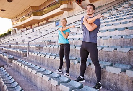 Foto de Fitness, brazos y pareja estirándose en el estadio para correr, maratón o entrenamiento de competición para la salud. Deportes, energía y atletas corredores con ejercicio de calentamiento para hacer ejercicio cardiovascular en pista - Imagen libre de derechos
