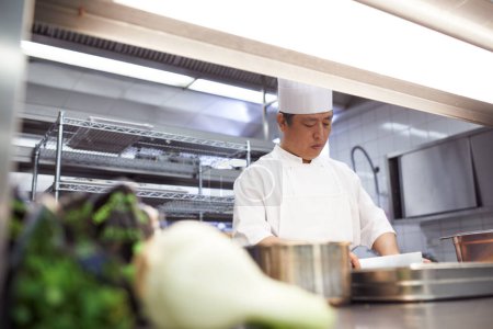 Professional, chef and asian man in kitchen for catering, cooking and serving food in restaurant. Business, culinary or male expert with cookware for hospitality, service and culinarian in uniform.
