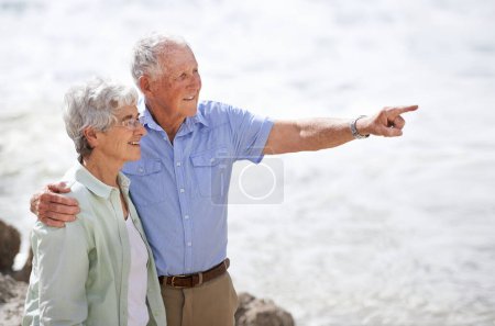 Téléchargez les photos : Aîné, couple et point à la plage avec le sourire pour les vacances de retraite ou anniversaire pour se détendre avec amour, vue et engagement avec le soutien. Homme âgé, femme et ensemble par l'océan pour la paix en vacances. - en image libre de droit