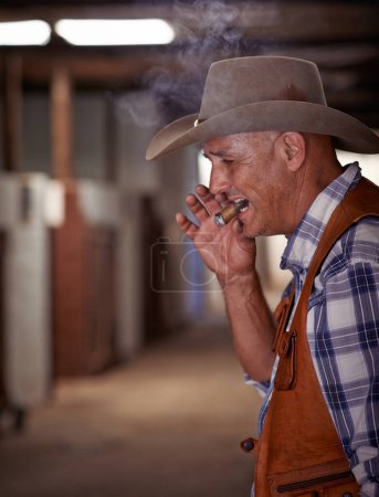 Foto de Humo, cigarro y vaquero mayor en el rancho para la agricultura, la agricultura y el cuidado de los animales de rodeo. Agricultor maduro, hombre y ranchero con cigarrillo, tabaco y tabaco en Texas. - Imagen libre de derechos