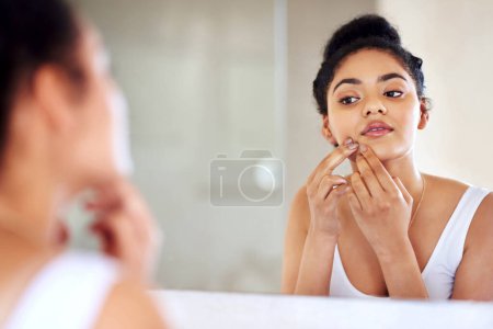 Photo for Skincare, woman and mirror to pop pimple on face with hands, dirt or scar on skin in home. Dermatology, facial wellness and girl in bathroom to squeeze acne, checking reflection or morning routine. - Royalty Free Image