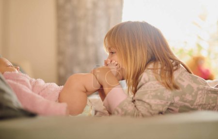 Photo for Family, feet and sister kissing baby girl on bed in home together for care, relationship or support. Bedroom, children and love with sibling kids bonding in apartment for child development or growth. - Royalty Free Image