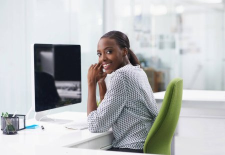Foto de Retrato, pantalla de ordenador y sonrisa con mujer negra de negocios en el escritorio en la oficina para la administración de la empresa. Mostrar, internet e informar con el joven empleado feliz en el escritorio en el lugar de trabajo para la investigación. - Imagen libre de derechos