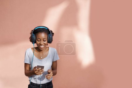 Photo for Girl, headphones and phone for song in studio, website and online for streaming playlist on pink background. Black female person, mockup space and internet for social media, kpop and app for music. - Royalty Free Image