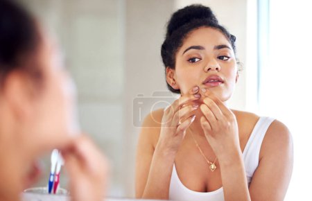 Photo for Skincare, reflection and woman popping pimple on face with hands, dirt or scar on skin in home. Dermatology, facial wellness and girl in bathroom to squeeze acne, checking mirror or morning routine. - Royalty Free Image