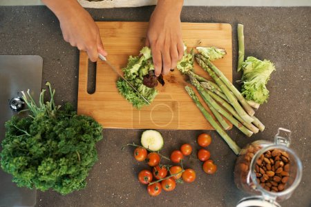 Téléchargez les photos : Mains, couteau et au-dessus pour les légumes dans la cuisine avec hachage, asperges et cuisine avec nutrition pour le dîner. Chef, personne et préparation des repas avec régime végétalien pour la nourriture, le bien-être et le déjeuner dans l'appartement. - en image libre de droit