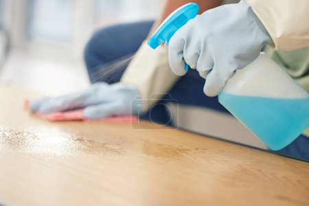 Photo for Cleaning, hands in gloves and spray at table in living room of home for domestic chores or housework. Bacteria, bottle and product to wipe with person in apartment for disinfection or housekeeping. - Royalty Free Image