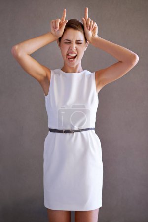 Photo for Woman, portrait and hand for horn in gray background, silly face and playful body language on studio. Female person, humor and funny expression for communication or emotion or symbol for mocking. - Royalty Free Image