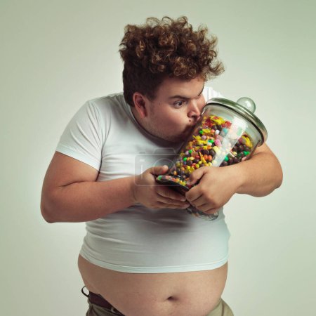 Photo for Love, candy and plus size man kissing glass jar in studio on gray background for craving or hunger. Food, obsession or possessive and crazy young person with lots of sugar for unhealthy eating. - Royalty Free Image