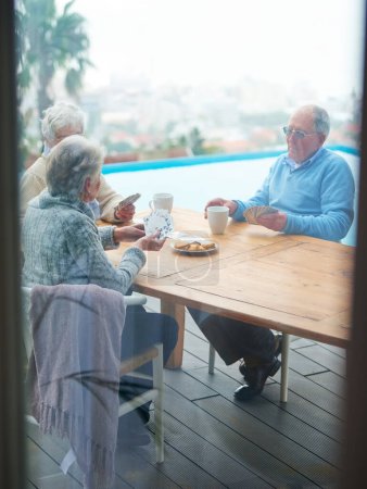 Photo for Senior people, friends and play cards at table at home, bonding or eating cookies to relax at patio outdoor. Elderly group, poker and game together for retirement, social gathering or drinking coffee. - Royalty Free Image