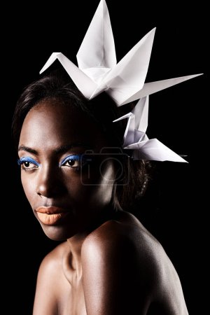 Téléchargez les photos : Studio, beauté et cosmétiques pour femme noire avec maquillage en fond sombre avec esthétique pour le luxe. Fard à paupières, lueur et fond de teint sur le visage de la fille pour briller, femme africaine et origami. - en image libre de droit
