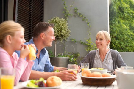 Photo for Family, lunch and happy with child on patio with conversation, relax and eating in summer at house. Parents, kid and outdoor for brunch, food and smile for talking with bonding, connection and love. - Royalty Free Image