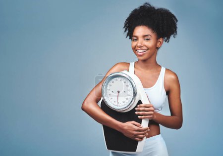 Foto de Chica negra, retrato y escala en el estudio para medir la pérdida de peso, fondo seguro y azul. Persona femenina, fitness y dieta para el equilibrio, espacio de maqueta y orgulloso de éxito de pérdida de peso y salud. - Imagen libre de derechos