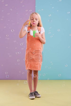 Photo for Fun, playing and kid blowing bubbles in studio with activity for child development and hobby. Youth, toy and young girl model with casual, cool and trendy style isolated by color block background - Royalty Free Image