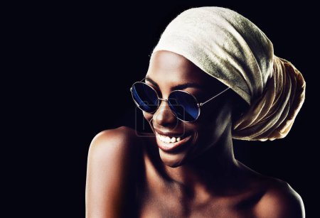 Foto de Mujer feliz, negra y gafas de sol con bufanda para la moda o el estilo en un fondo de estudio oscuro. Joven mujer africana o modelo con sonrisa, sombreros y gafas para accesorios elegantes en maqueta. - Imagen libre de derechos