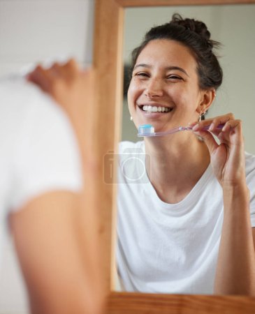 Téléchargez les photos : Woman, toothbrush and smile by mirror in morning to start routine for hygiene, health or oral wellness. Girl, person and toothpaste in reflection to check results, teeth whitening and mouth in home. - en image libre de droit