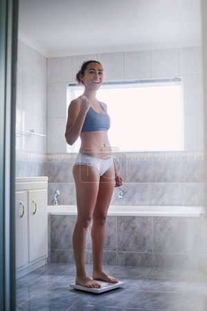 Photo for Weight loss, woman and happy in bathroom on scale with yes, proud and standing in underwear for goals. Female person, success and diet at home for nutrition, fitness and achievement or checking BMI. - Royalty Free Image