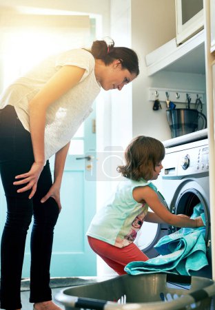 Photo for Help, home and mom with kid at washing machine for chores, teaching and learning housekeeping routine. Laundry, mother and daughter cleaning clothes together with support, care and child development - Royalty Free Image