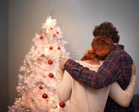 Photo for Couple, hug and Christmas tree for holiday celebration in evening with light decoration, bonding or connection. Man, woman and back for winter vacation for gift giving or festive season, love or care. - Royalty Free Image
