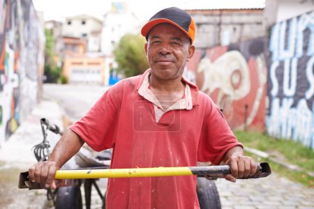 Foto de Hombre, retrato y carro de basura en la calle para sonreír, caminar y recoger basura para reciclar para la ecología. Persona, rickshaw o carretilla para la sostenibilidad, el medio ambiente y la naturaleza en la carretera en Sao Paulo. - Imagen libre de derechos