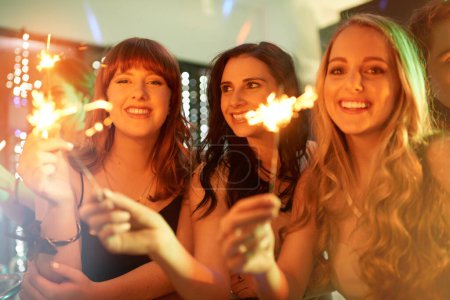 Photo for Group, friends and celebration with sparklers, women and cheerful at party, night out and fireworks. Happy, event and smile for new year, birthday and club in disco, lights and entertainment. - Royalty Free Image
