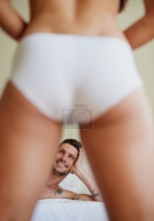 Téléchargez les photos : Man smiling, couple and sexy legs in bedroom for striptease, seduction and kinky at home. Male person, excited and butt in panties for intimacy, playful or affection in motel or hotel for making love. - en image libre de droit