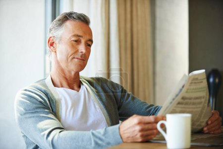 Photo for Mature, man and newspaper for reading in house, relax and information or articles in morning with coffee. News, breakfast table and rest and calm for entertainment pages, current events in apartment. - Royalty Free Image