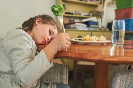 Photo for Angry, child and eating healthy food in home with vegetables, nutrition and tired of green diet. Hungry, kid and frustrated with plate of broccoli, salad and dislike for vegan dinner or choice. - Royalty Free Image