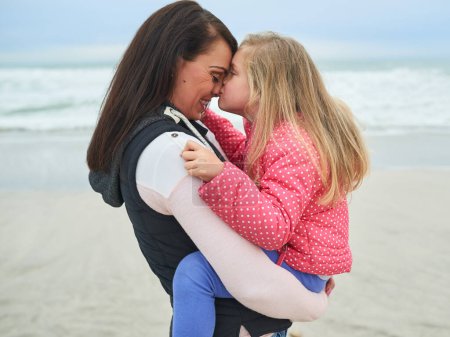 Téléchargez les photos : Embrassez mère, fille et câlin sur la plage pour l'amour, les soins et la détente à l'océan en Australie. Mère célibataire, fille et affection au bord de la mer pour la sécurité, la fête des mères et le soutien dans la nature tout en étant heureux dans le froid. - en image libre de droit