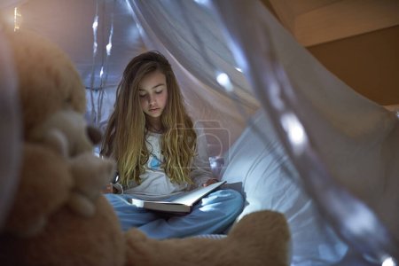 Photo for Night, girl and blanket fort for reading book, learning or education for childhood development. Home, child and fairytale with storytelling, relax or fantasy for entertainment or knowledge in house. - Royalty Free Image