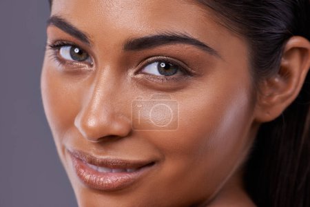Téléchargez les photos : Portrait, soins de la peau et la beauté de la femme heureuse dans le maquillage, lueur ou brillance isolé sur fond de studio gris. Visage, gros plan et modèle indien en cosmétique dans le traitement facial spa, dermatologie ou santé. - en image libre de droit