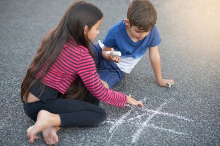 Photo for Chalk, road and kids with game, playing and outdoor in playground of preschool, summer and concentration. Creative, boy and girl in street, hopscotch and pavement for break in weekend and together. - Royalty Free Image