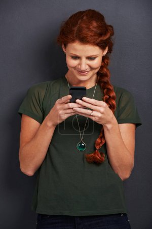 Photo for Smile, reading and woman in studio with phone for social media, online chat or networking. Communication, internet and happy girl with smartphone, typing and scroll on mobile app with dark background. - Royalty Free Image