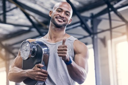 Photo for Portrait, scale and thumbs up with bodybuilder man in gym for strength training or workout. Exercise, smile and success with happy athlete in health club for motivation, support or thank you. - Royalty Free Image