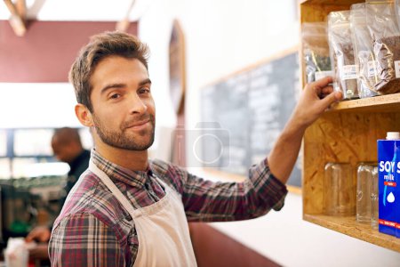 Téléchargez les photos : Homme, barista et portrait par une étagère dans un café avec sourire pour le service, la recherche et les ingrédients pour boire. Serveur, personne ou propriétaire de petite entreprise dans un café avec produit, haricots et heureux pour le choix. - en image libre de droit