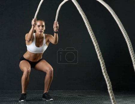Photo for Woman, studio and training with rope for exercise, calorie burn and body workout for vitality or wellness. Girl, squat and cardio fitness on black background for strength, power and endurance or gym - Royalty Free Image