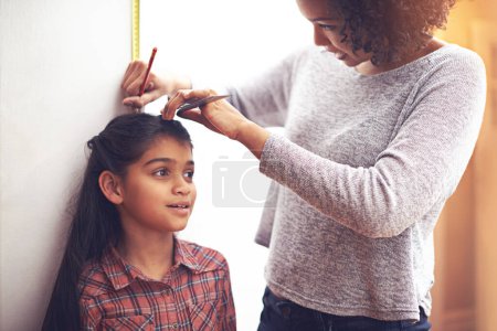 Photo for Mother, child and measuring height with ruler at wall for growth development in home for childhood, love or bonding. Female person, daughter and pencil in apartment for size checking, youth or parent. - Royalty Free Image