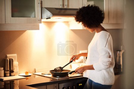 Photo for Black woman, pan and cooking on stove in home, frying and meal preparation in kitchen. Female person, apartment and nutrition in food, diet and wellness for cuisine on gas for dinner routine in house. - Royalty Free Image