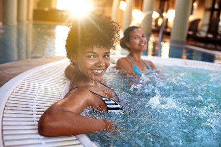 Photo for Excited woman, portrait and relax with water in jacuzzi at hotel, resort or hot tub spa together. Happy female person or friends with smile for relaxation, hospitality or heated bath by indoor pool. - Royalty Free Image