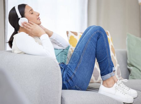 Photo for Headphones, music and woman on sofa in home for relaxing, resting and chill on weekend. Happy, smile and person on couch listening to audio, song and radio on streaming subscription in living room. - Royalty Free Image