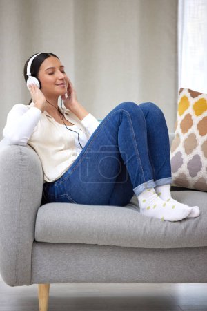 Photo for Headphones, happy and woman on sofa in home for relaxing, resting and chill on weekend. Music, smile and person on couch listening to audio, song and radio on streaming subscription in living room. - Royalty Free Image