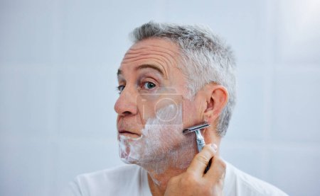 Mature man, razor and shaving cream in home, beauty and tool or soap for skincare grooming in routine. Person, blade and cleaning or facial treatment for cosmetics, self care maintenance and hygiene.