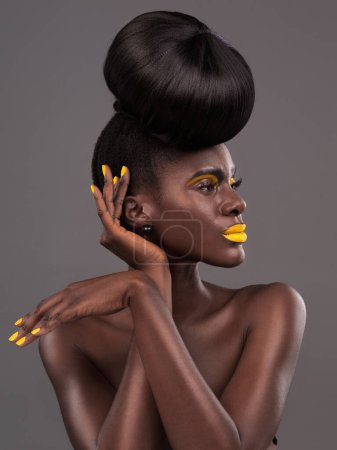 Foto de Africano, modelo y cara de estudio con creativo, belleza y lápiz labial amarillo cosmético. Desnuda, mujer y piel con confianza, pelo dramático y moño para el glamour o maquillaje de moda aislado sobre fondo gris. - Imagen libre de derechos